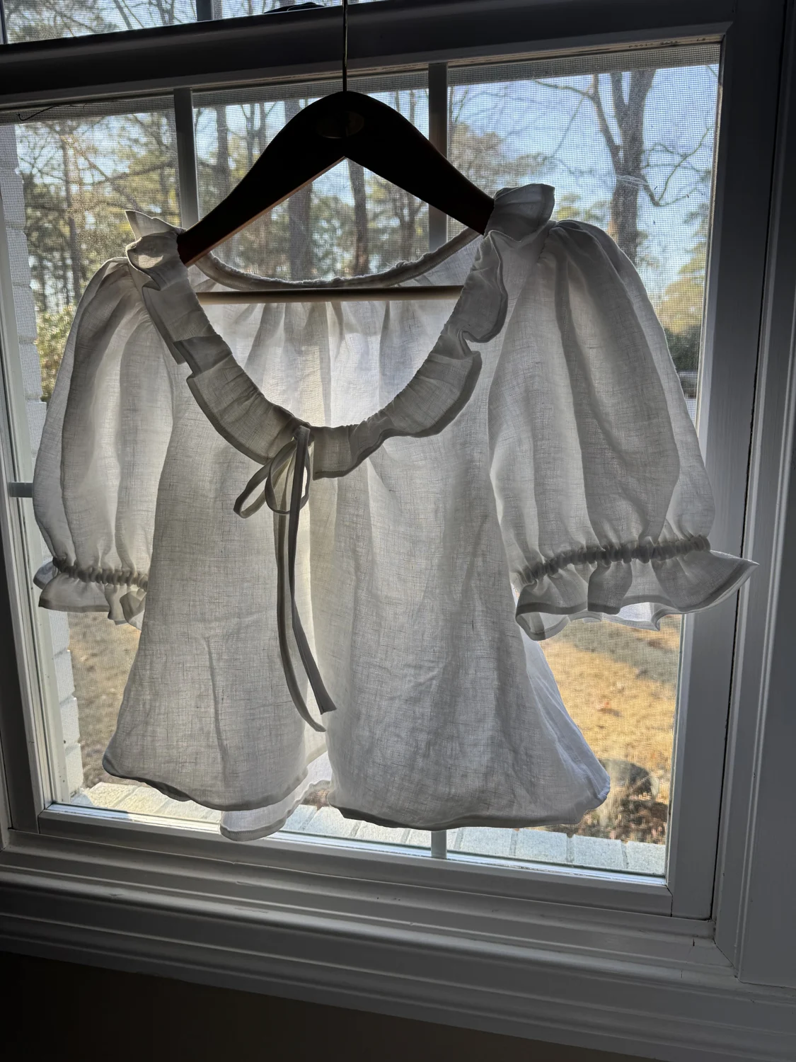 Handmade sheer blouse with a ruffled collar hanging in a window